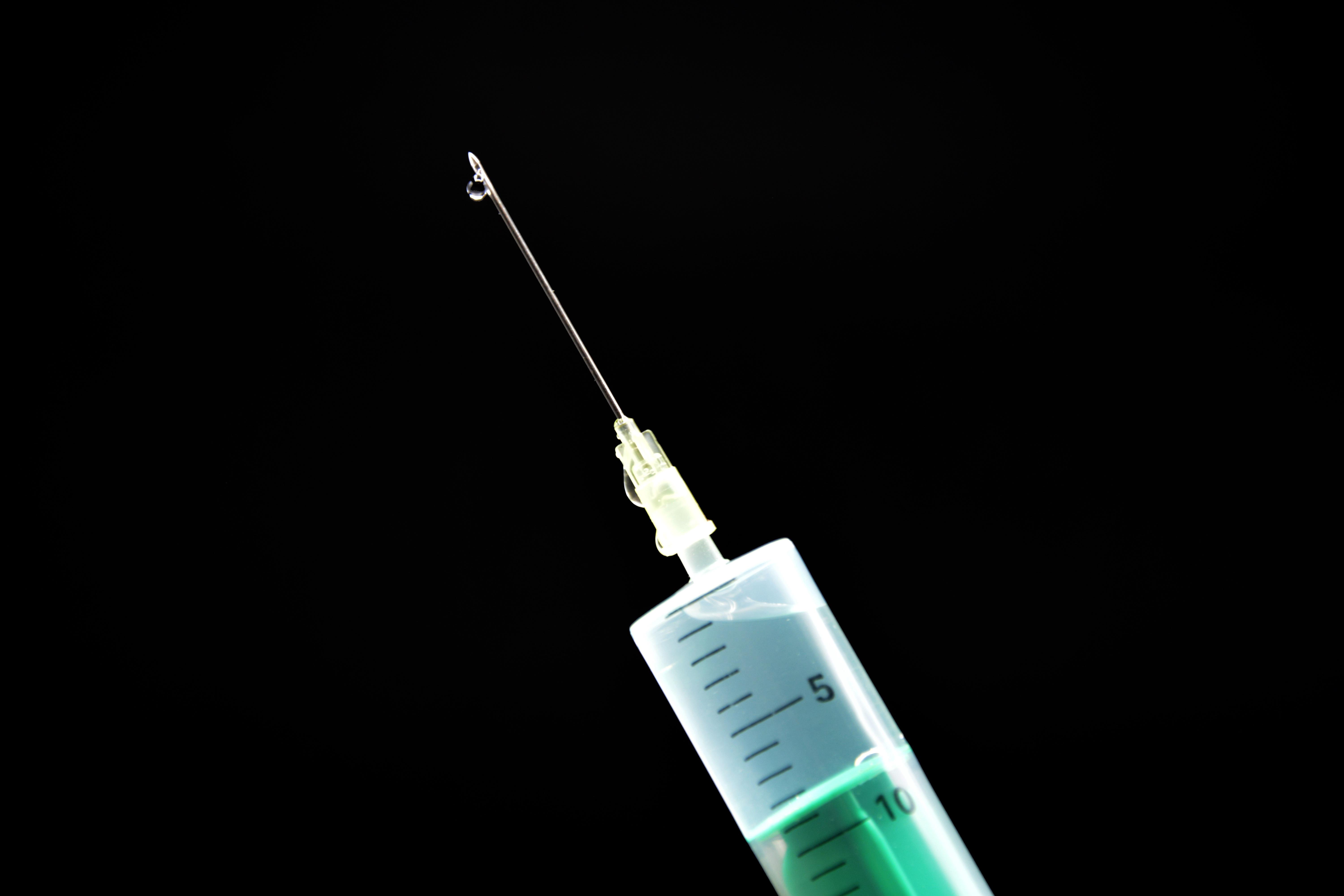 syringe filled with clear liquid with a drop on the needle