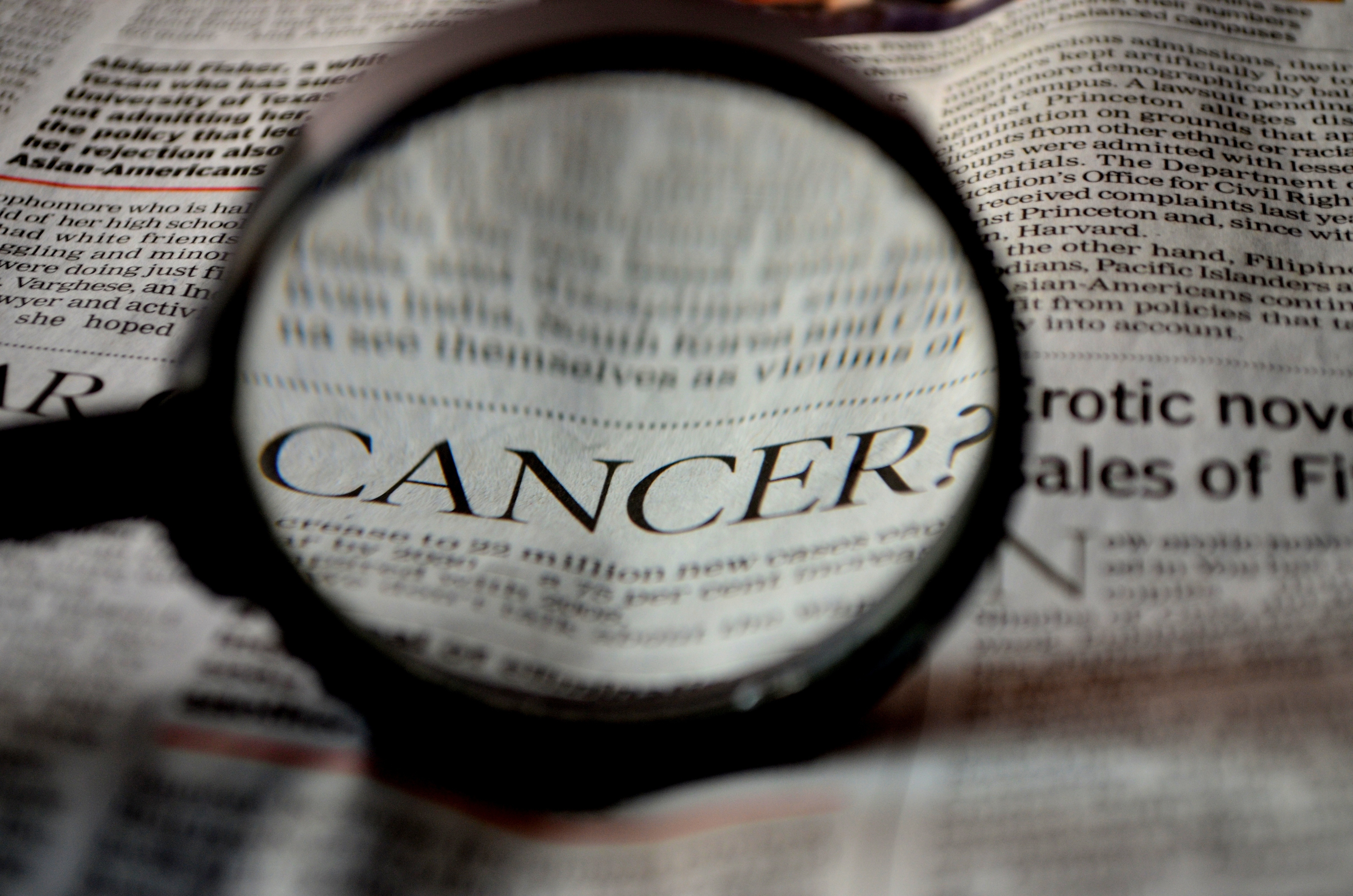 Magnifying glass over the word cancer in a newspaper headline